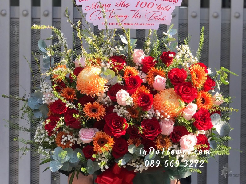 G03241397 GIỎ HOA MỪNG THỌ 100 TUỔI thiết kế tone màu đỏ cam, chủ đạo Hoa Hồng Đỏ Ecuador, Cúc Mẫu Đơn Cam