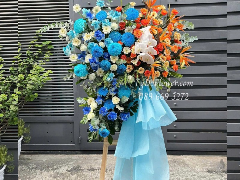 KCM0625490 KỆ HOA CHÚC MỪNG KHAI TRƯƠNG Thiết kế gam màu cam xanh dương, chủ đạo hoa Cúc Mẫu Đơn Xanh Dương, Cam Sprit Roses, Thiên Điểu
