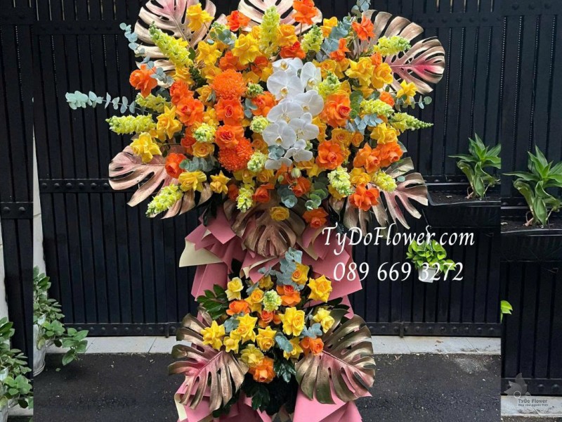 KCM0825612 KỆ HOA CHÚC MỪNG Thiết kế gam màu vàng cam, chủ đạo hoa hồng, lan hồ điệp, lá trầu bà nam mỹ
