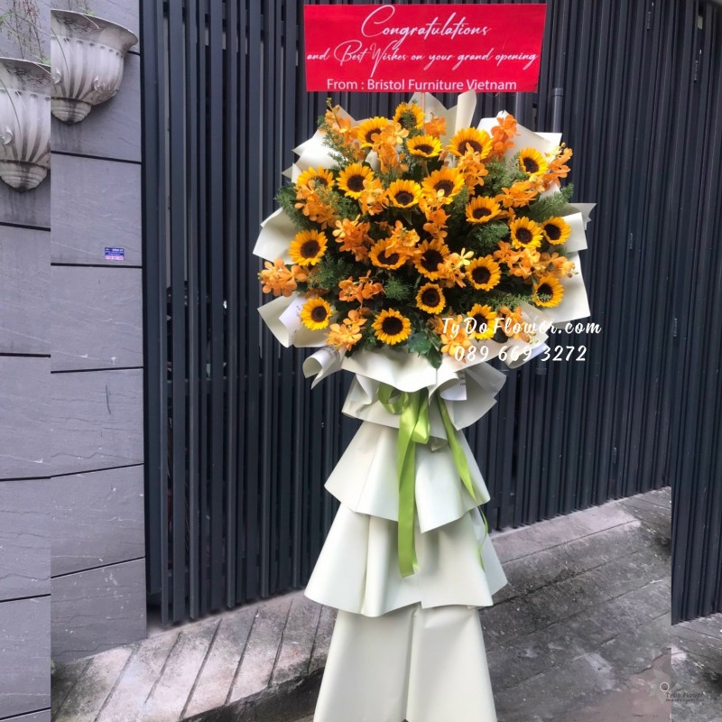 KCM09231032 KỆ HOA CHÚC MỪNG KHAI TRƯƠNG thiết kế Hoa Hướng Dương, Hoa Lan Mokara Vàng mix lá xanh