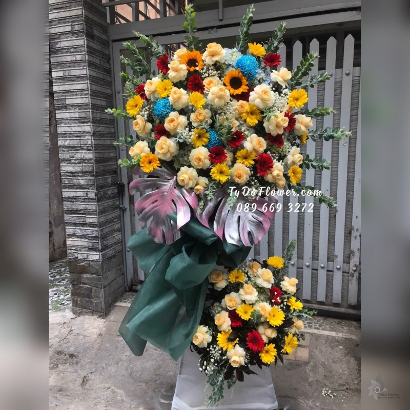 KCM01241292 KỆ HOA CHÚC MỪNG thiết kế tone màu đỏ vàng xanh, chủ đạo Hoa Hồng Juliet, điểm nhấn Cúc Mẫu Đơn Xanh Dương