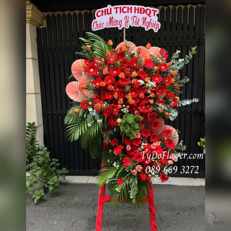 KCM0825609 KỆ HOA CHÚC MỪNG LỄ TỐT NGHIỆP Thiết kế hoa hồng cam, đồng tiền đỏ, phụ kiện trang trí cao cấp