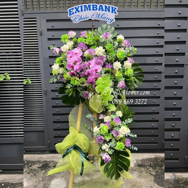 KCM0825611 KỆ HOA CHÚC MỪNG Thiết kế gam màu tím xanh bơ, chủ đạo hoa hồng, lan hồ điệp, wicky, lá trầu bà nam mỹ